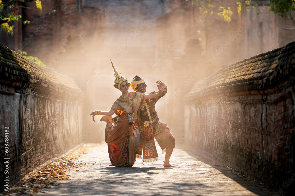 Fototapeta premium Beautiful Asian woman wear Thai traditional dress action of dancing together with Thai classic masked from the Ramakien character as black monkey with ancient wall and buildin in mist background.
