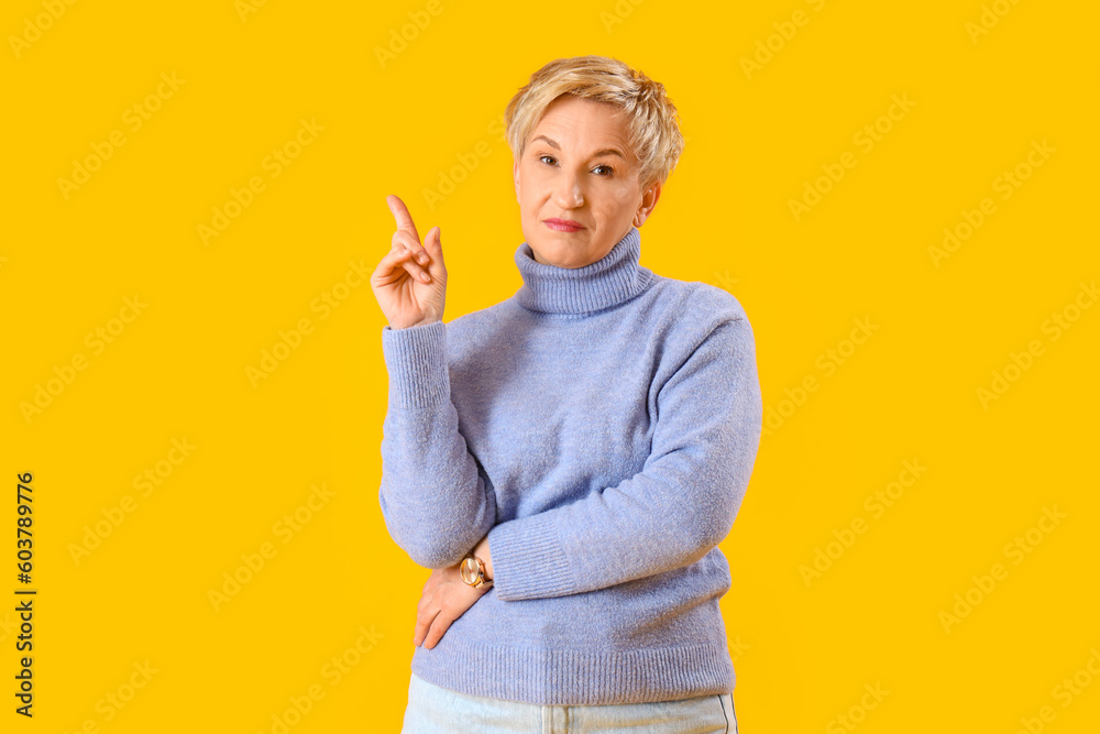 Thoughtful mature woman pointing at something on yellow background Thoughtful mature woman pointing at something on yellow background
