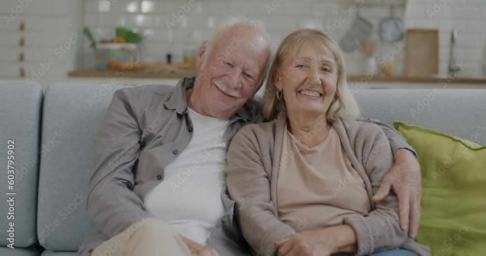 Portrait of beautiful senior couple smiling and laughing sitting on couch and hugging at home. Committed retationship and retirement concept. Portrait of beautiful senior couple smiling and laughing sitting on couch and hugging at home. Committed retationship and retirement concept.