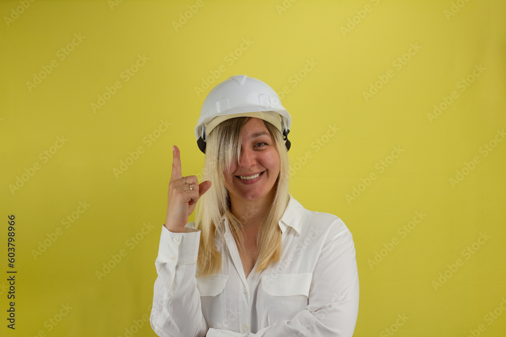 A smiling woman in a construction helmet raised her index finger up. The female engineer had an idea. Isolated on a yellow background. The concept of an engineer solves a problem.