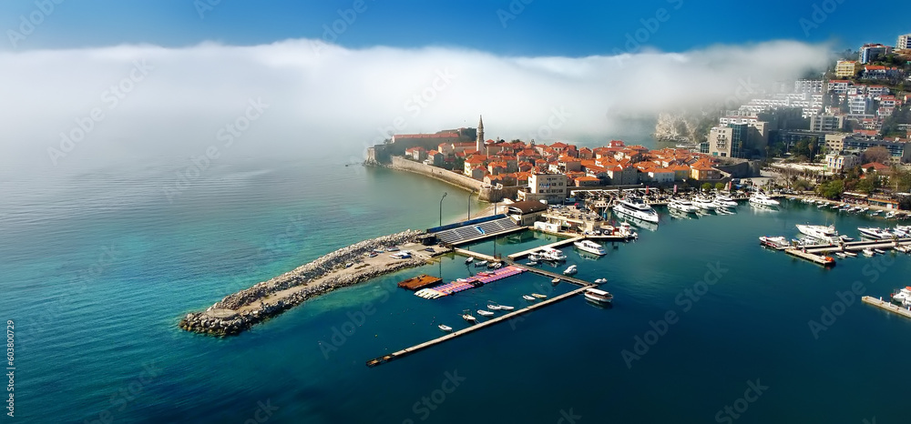Mysterious panoramic drone view of the ancient city of Budva during heavy cloud cover. Old medieval city with red roofs in Montenegro on the sunset. Banner