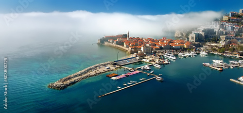 Mysterious panoramic drone view of the ancient city of Budva during heavy cloud cover. Old medieval city with red roofs in Montenegro on the sunset. Banner