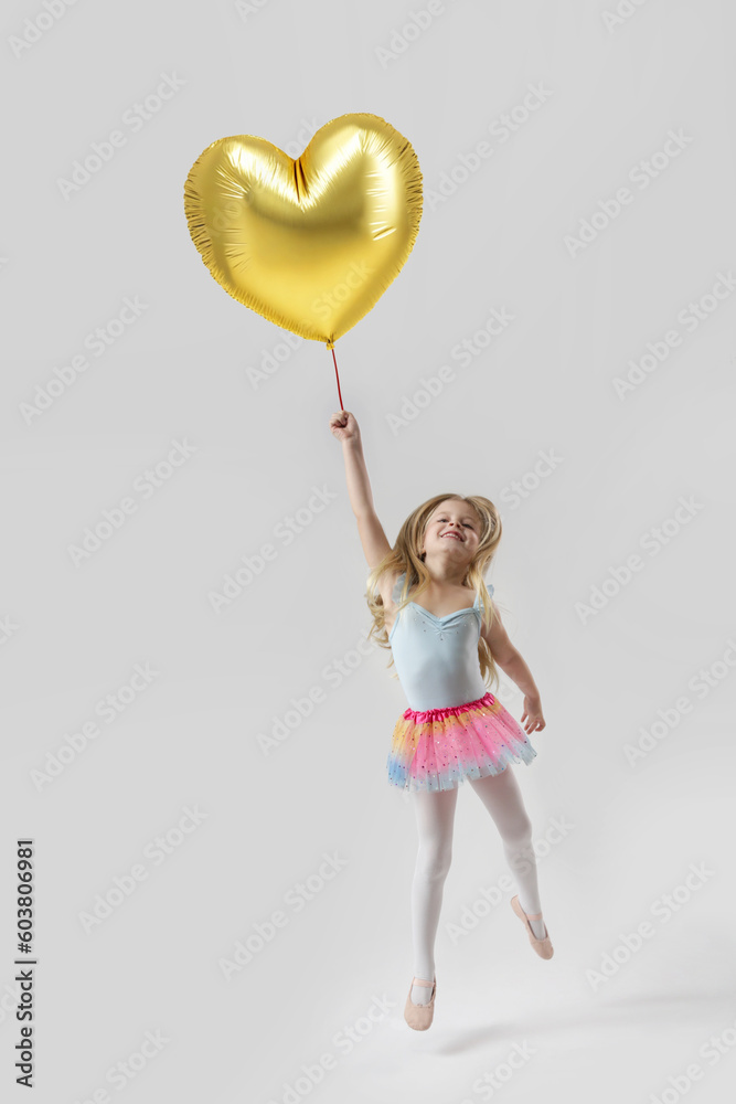 Studio portrait of adorable little girl holding large golden heart shaped balloon