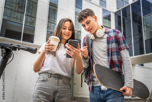 Two teenagers with headphones and skateboard looking at mobile phone and having fun, modern lifestyle concept