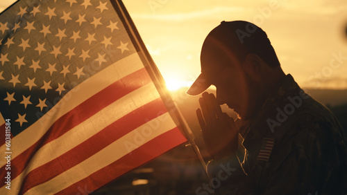 Silhouette of American soldier praying for memorial day against the flag outdoor