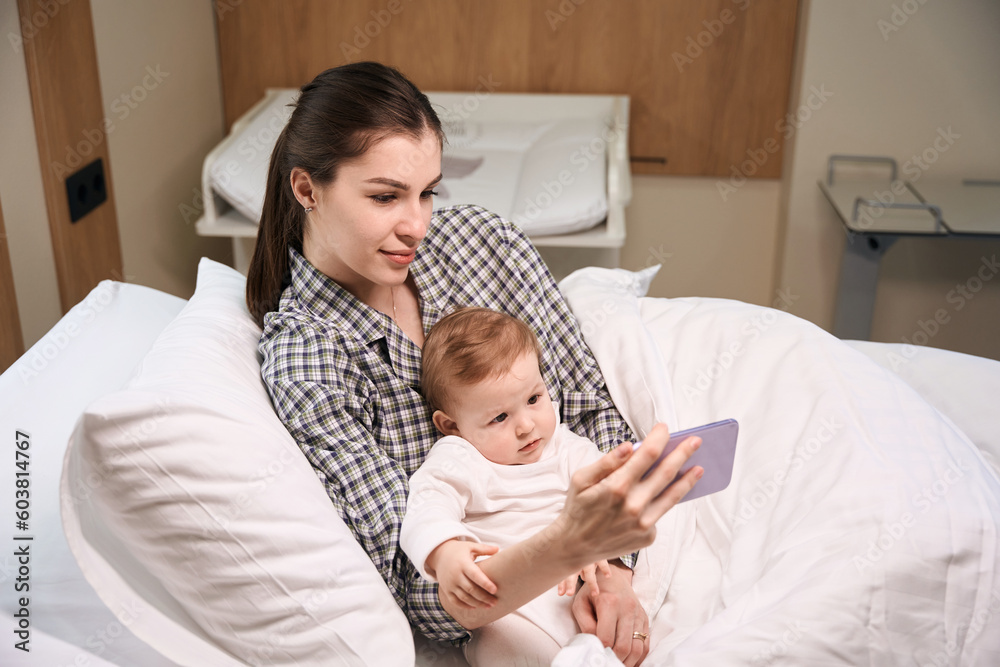 Mother and ill child watching video on smartphone in hospital room Mother and ill child watching video on smartphone in hospital room