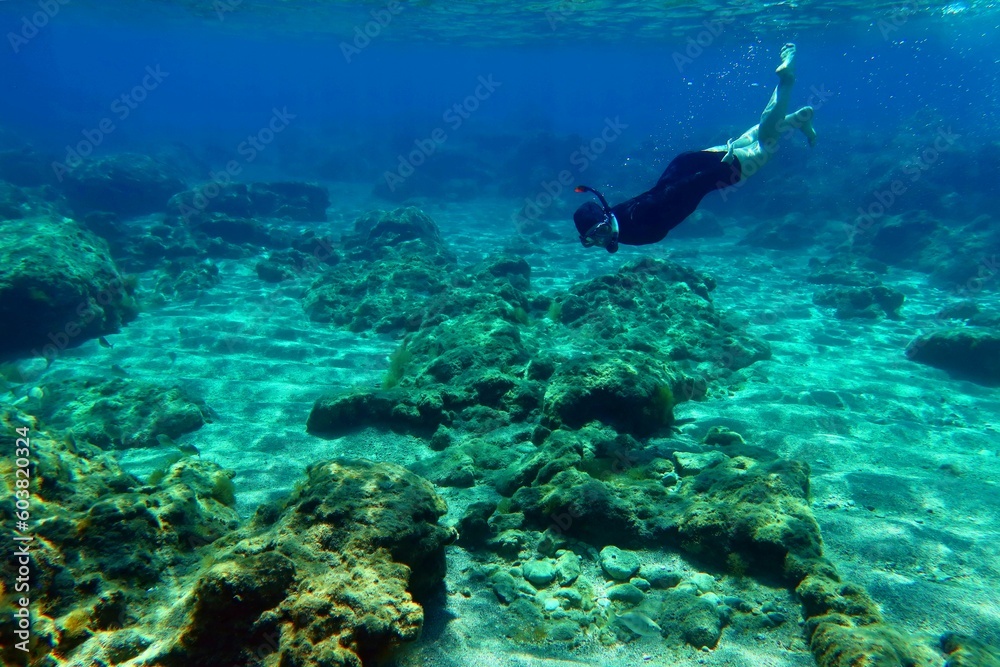 Girl snorkeling in the ocean. Swimming and diving in the sea. Activity in the water, young woman with mask and snorkel. Underwater seascape with sandy bottom, fish and blue water.