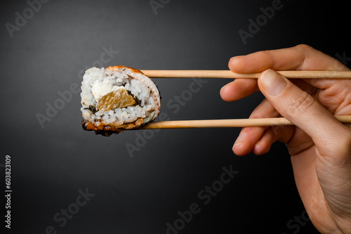 Man's hand holds Philadelphia sushi roll with smoked eel, salmon and cream cheese with bamboo chopsticks