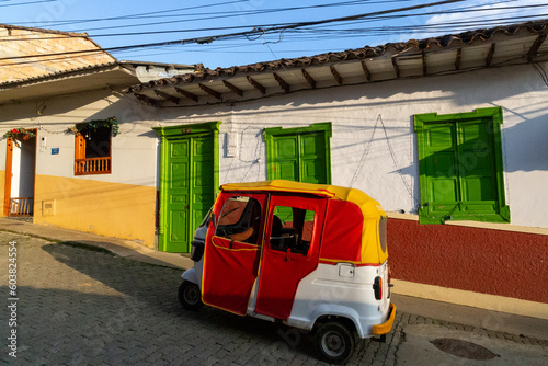 little motorbike, little red three-wheeled car next to a colorful house in latin america