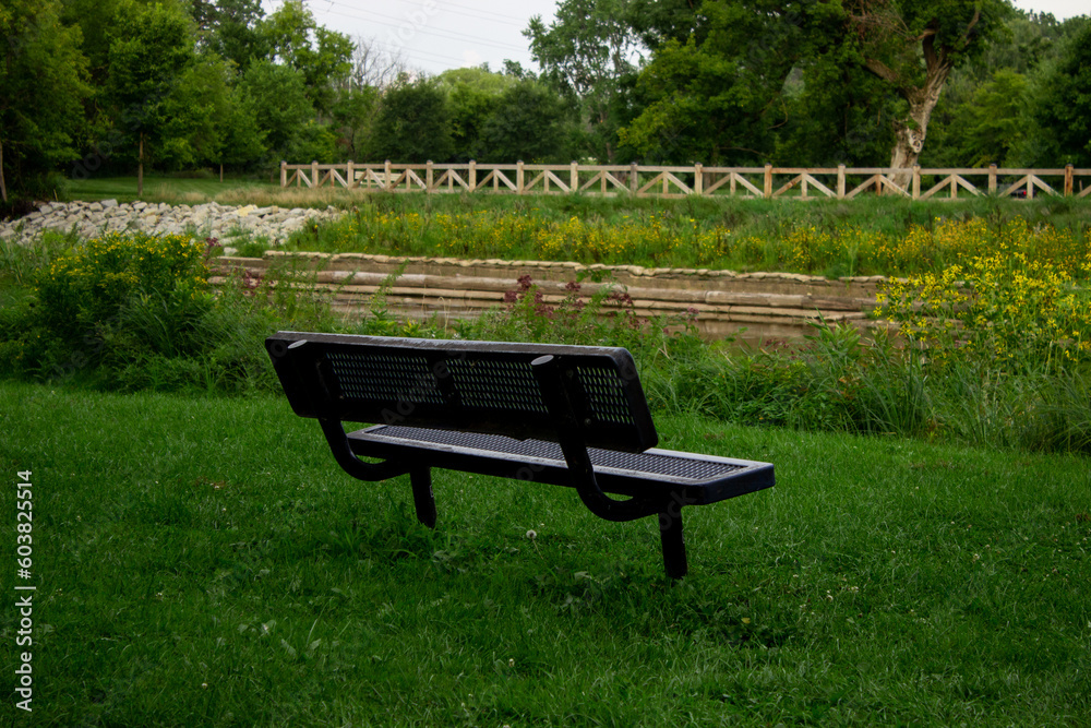 Bench in the park overlooking the river, green grass, and wooden fence