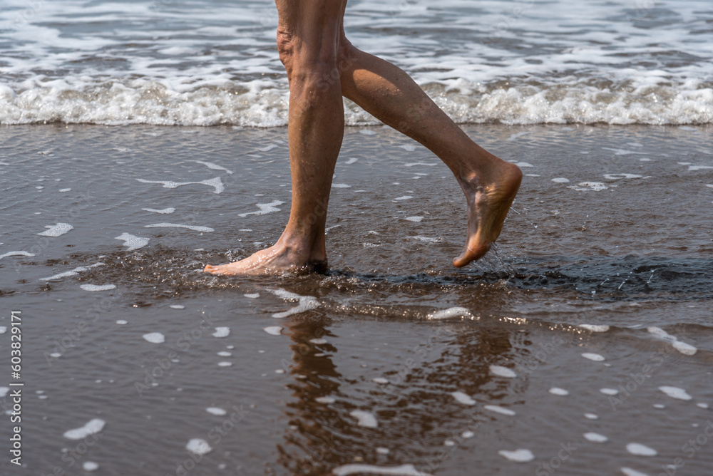 Barefoot woman walking on the seashore at the beach.