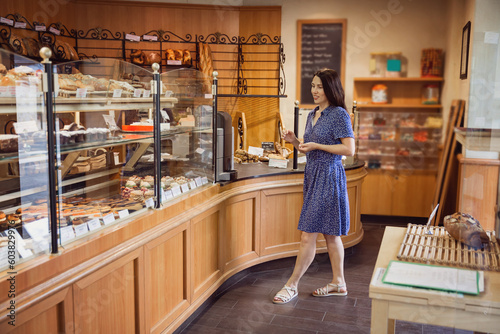 Young pretty woman shopping in a bakery. A customer standing near a showcase with sweets in a store
