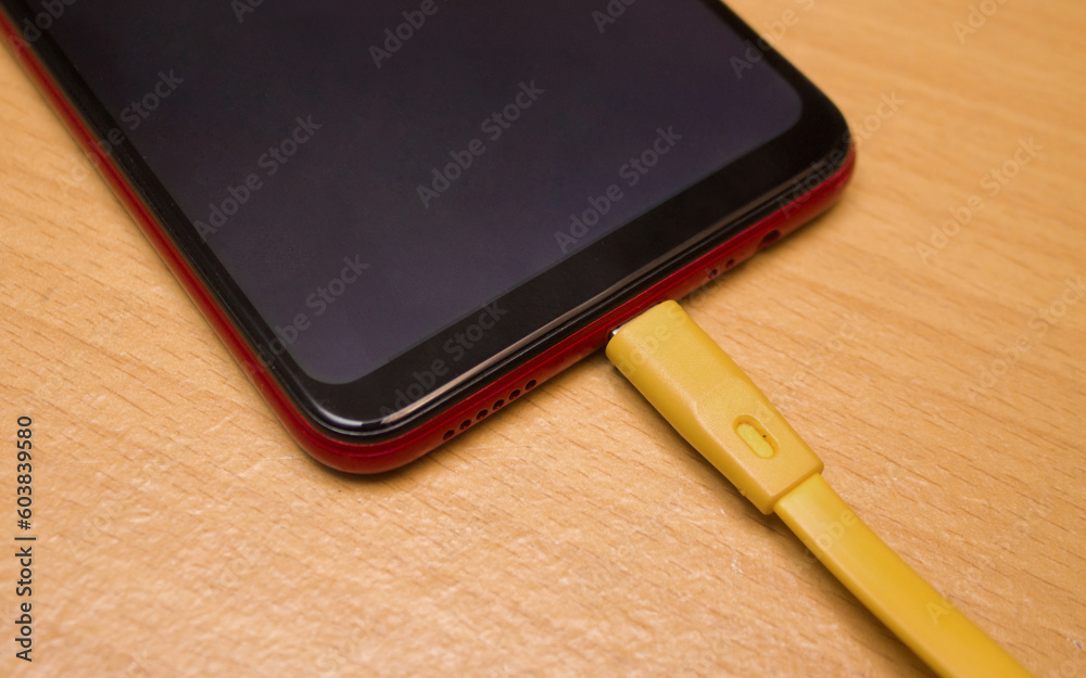 A smartphone in charge on a wooden table A smartphone in charge on a wooden table
