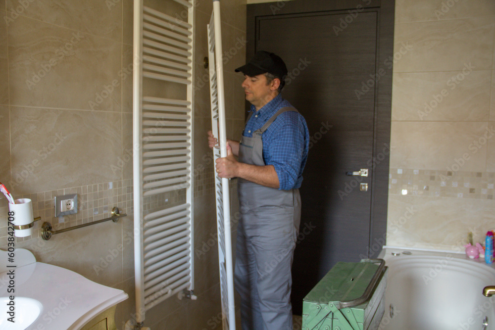 Image of a plumber while he is assembling a radiator like a towel warmer in a bathroom at home.
