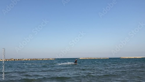 Panning view in Porto San Giorgio at a black and green kitesurfer heading towards the coast of The Adriatic Sea in Porto San Giorgio, jumping, pirouetting and going back towards the deeper blue water