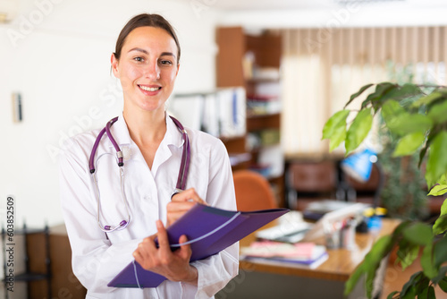 Portrait of friendly female doctor wearing uniform with folder