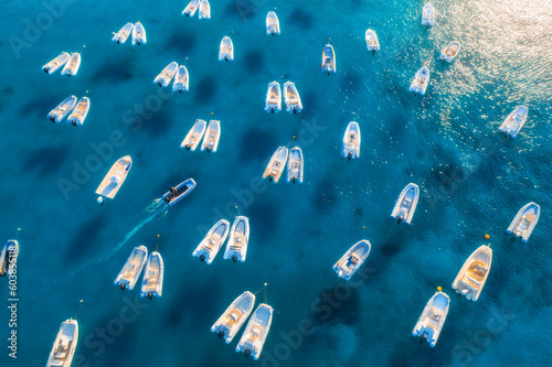 Aerial view of many motorboats on blue sea at sunset in summer. Travel in Sardinia, Italy. Drone view from above of speed boats, yachts, ocean, transparent azure water. Tropical seascape