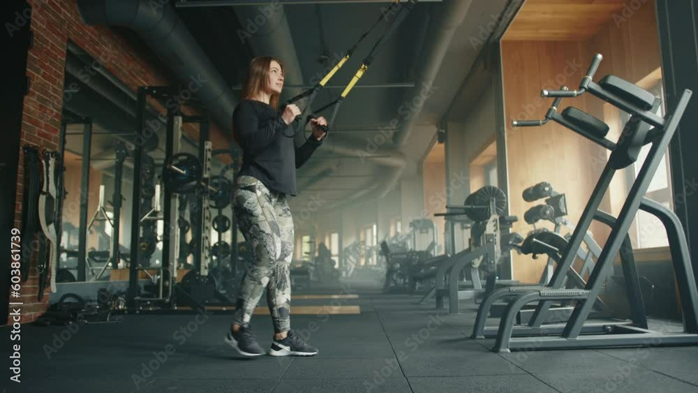 Profile shot of young athletic woman performing single leg squats on suspension trainer. Woman holds handles of suspension trainer and performs exercise. High quality 4k footage Profile shot of young athletic woman performing single leg squats on suspension trainer. Woman holds handles of suspension trainer and performs exercise. High quality 4k footage