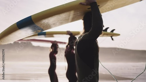 Young friends carrying surfboards walking talking on ocean beach. Active surfer sports women and man friends or family getting ready to practice in the sea, catch a wave on a high tide. 