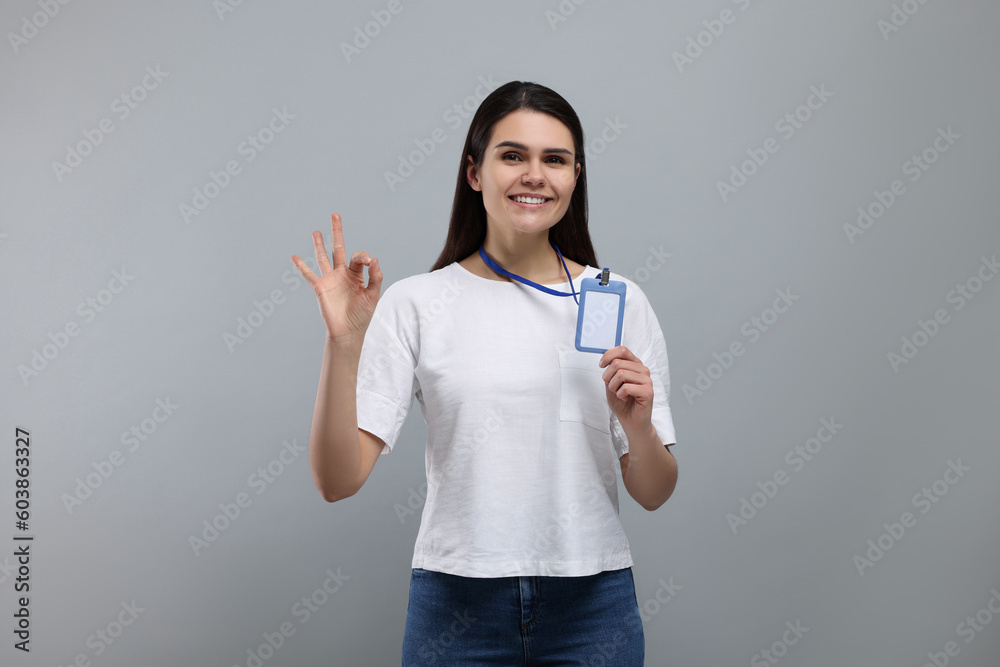 Smiling woman holding vip pass badge and showing ok gesture on grey background Smiling woman holding vip pass badge and showing ok gesture on grey background