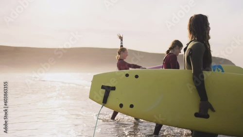 Young friends carrying surfboards walking talking on ocean beach. Active surfer sports women and man friends or family getting ready to practice in the sea, catch a wave on a high tide. photo