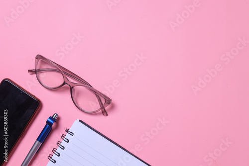 Minimal women office desk with notebook, pen, mobile phone and women's fashion galsses on pink background. Flat lay concept for magazines, websites, media.