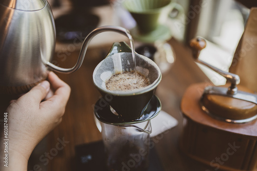 Professional hipster barista making drip brewing, filtered coffee or pour over coffee with hot water and filter paper in coffee shop cafe, black vintage tone of fresh caffeine aroma beverage