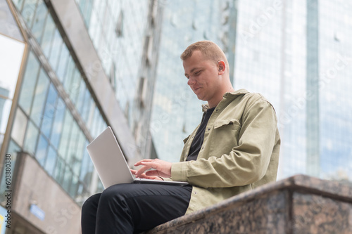 Sad guy with hearing aid using laptop outdoors. 