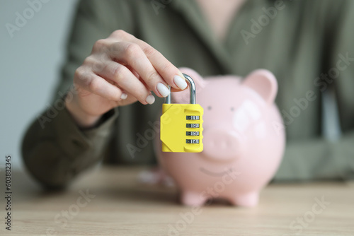 Woman holds combination padlock in front of piggy bank