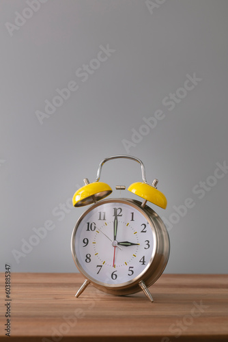 Retro silver alarm clock. 3:00. am, pm. Neutral background. Brown wood surface. Vertical photography with empty space for text or image.