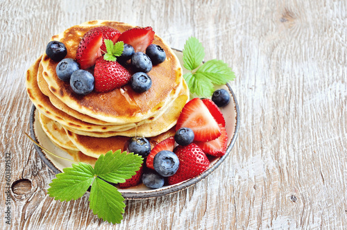 Stack of pancakes with fresh strawberries, blueberries, maple syrup and honey for breakfast, selective focus