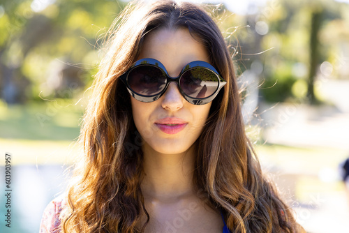 Portrait of smiling fit caucasian woman in sunglasses standing in sunny garden