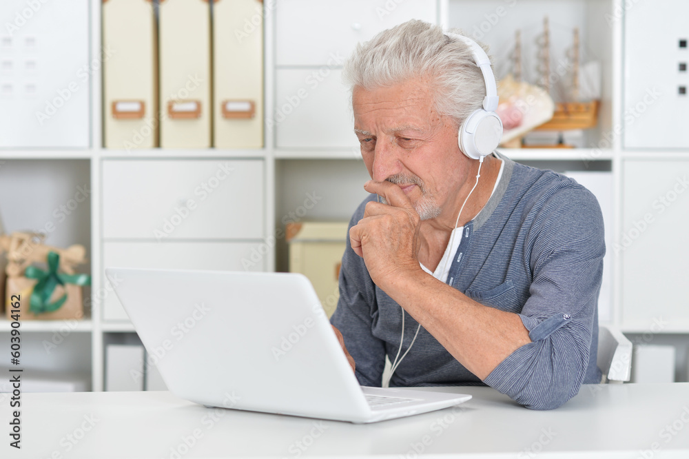 Thoughtful old man in headphones with laptop at home Thoughtful old man in headphones with laptop at home
