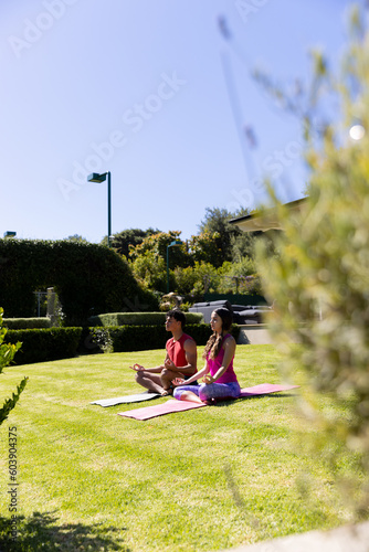 Happy diverse fit couple practicing yoga meditation sitting in sunny garden, with copy space