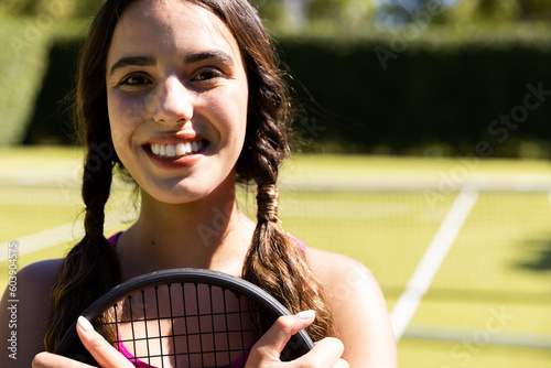 Portrait of happy fit caucasian woman holding tennis racket on outdoor tennis court, copy space