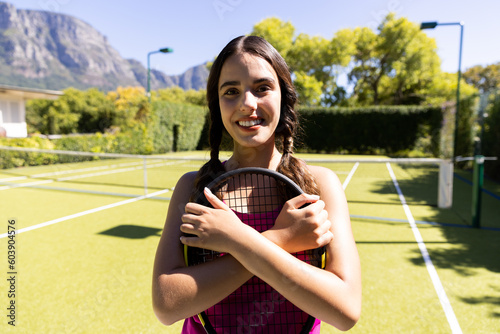 Portrait of happy fit caucasian woman holding tennis racket on sunny outdoor tennis court