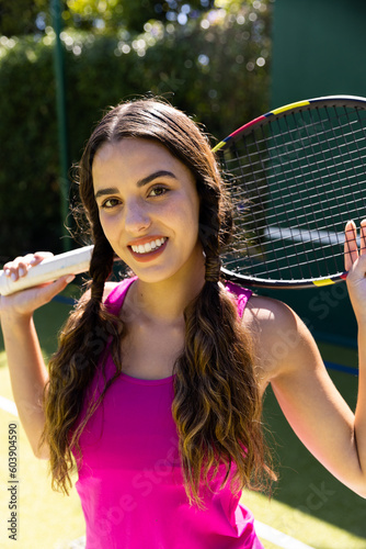 Portrait of happy fit caucasian woman holding tennis racket on sunny outdoor tennis court