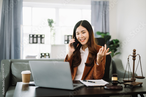 Asian female lawyer chatting online with client on laptop, smartphone discussing details of lawsuit. in modern office