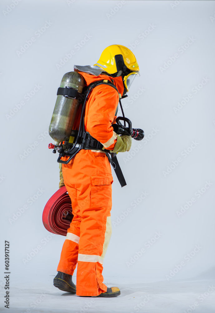 The professional firefighter is standing with his back turned holding a fire hose and wearing an oxygen tank on his back while looking down at the floor on a white background. The professional firefighter is standing with his back turned holding a fire hose and wearing an oxygen tank on his back while looking down at the floor on a white background.