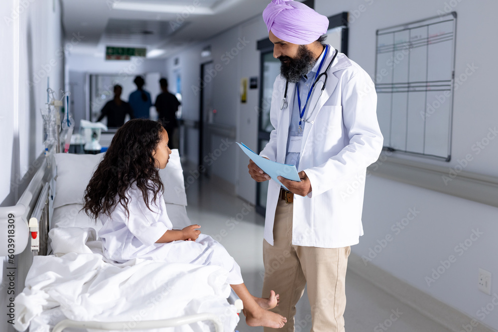 Happy sikh male doctor in turban and biracial girl patient talking in corridor at hospital Happy sikh male doctor in turban and biracial girl patient talking in corridor at hospital