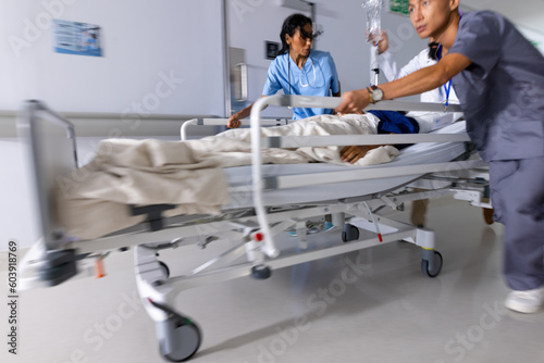 Diverse doctors urgently pushing patient lying in bed in corridor at hospital photo