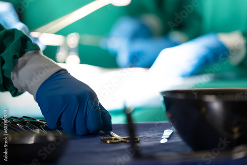 Gloved hand of surgeon picking up surgical tool during operation on patient in operating theatre photo