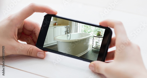 Composition of caucasian woman's hands holding smartphone with photo of bathroom