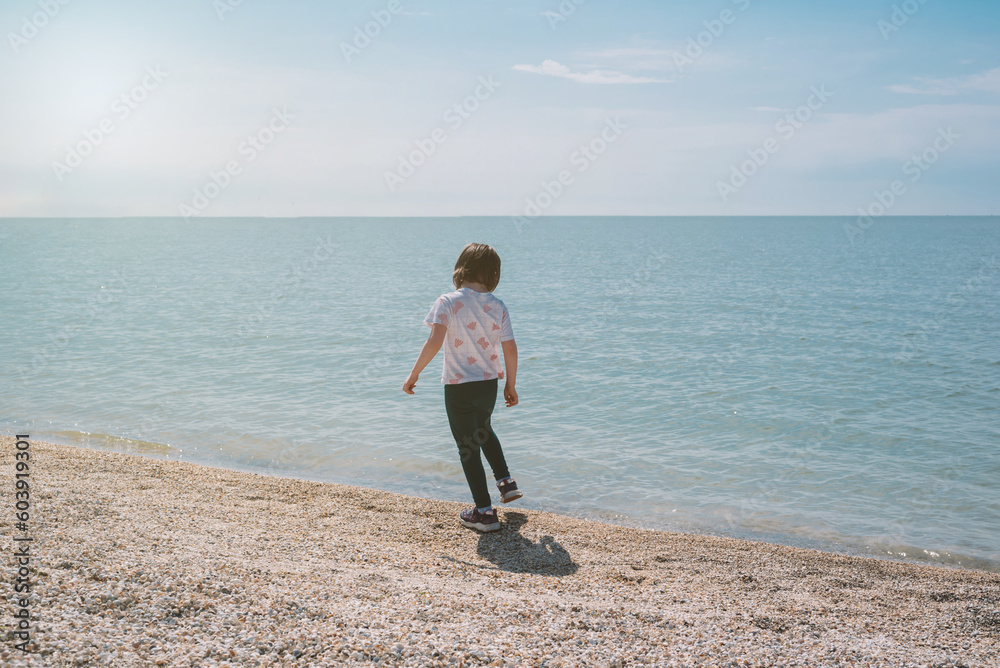 Girl walks along the seashore on a sunny day. Back view. International Children's Day concept, travel and holidays