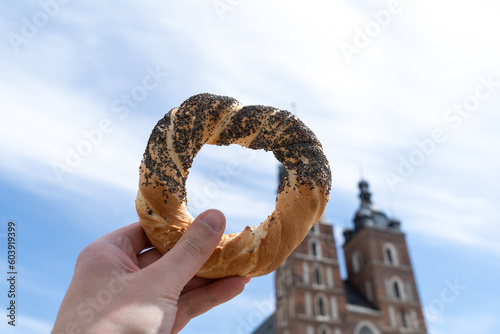 Hand holding obwarzanek krakowski pretzel on Cracow Main Market Square. St. Mary's Basilica, Bazylika Mariacka Kraków or Kościół Mariacki Church in bg. Krakowskie obwarzanki food in Krakow, Poland. photo