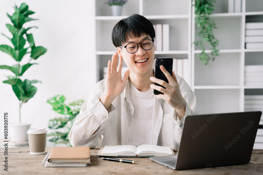 happy smiling Asian student waved to greet colleagues using a smartphone and laptop computer at home. happy smiling Asian student waved to greet colleagues using a smartphone and laptop computer at home.