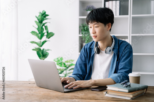 male student in casual clothes sitting at wooden table with laptop.