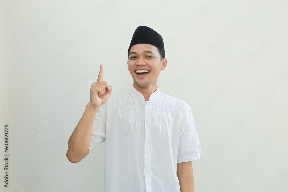 Excited young Asian Muslim man raising fists and celebrating victory on Ramadan isolated over white background. People religious Islam lifestyle concept Excited young Asian Muslim man raising fists and celebrating victory on Ramadan isolated over white background. People religious Islam lifestyle concept