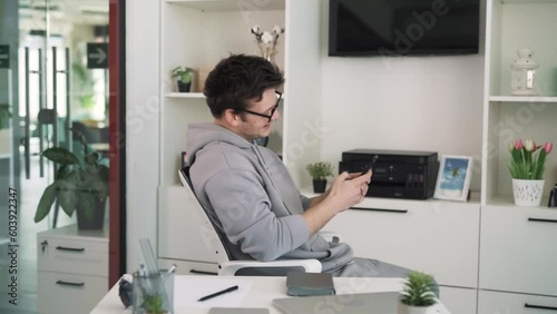 Wallpaper Mural The young man sits on a chair in front of a table in a bright office and is delighted as he reads on his phone. The man gesticulates emotionally, showing his joy. Torontodigital.ca