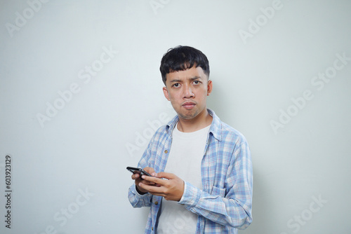 angry asian man facial expression using mobile phone looking at camera isolated on white background photo
